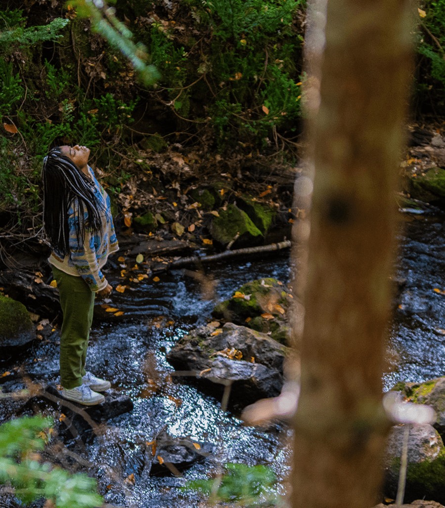 Person standing by a forest stream, serene.